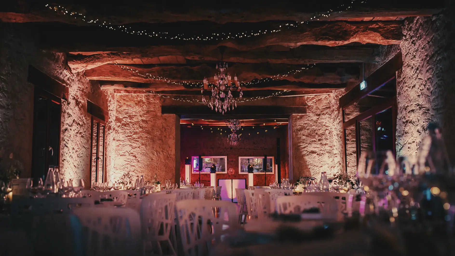 Salle de réception aux murs en pierre et poutres apparentes mis en valeur par un éclairage chaud