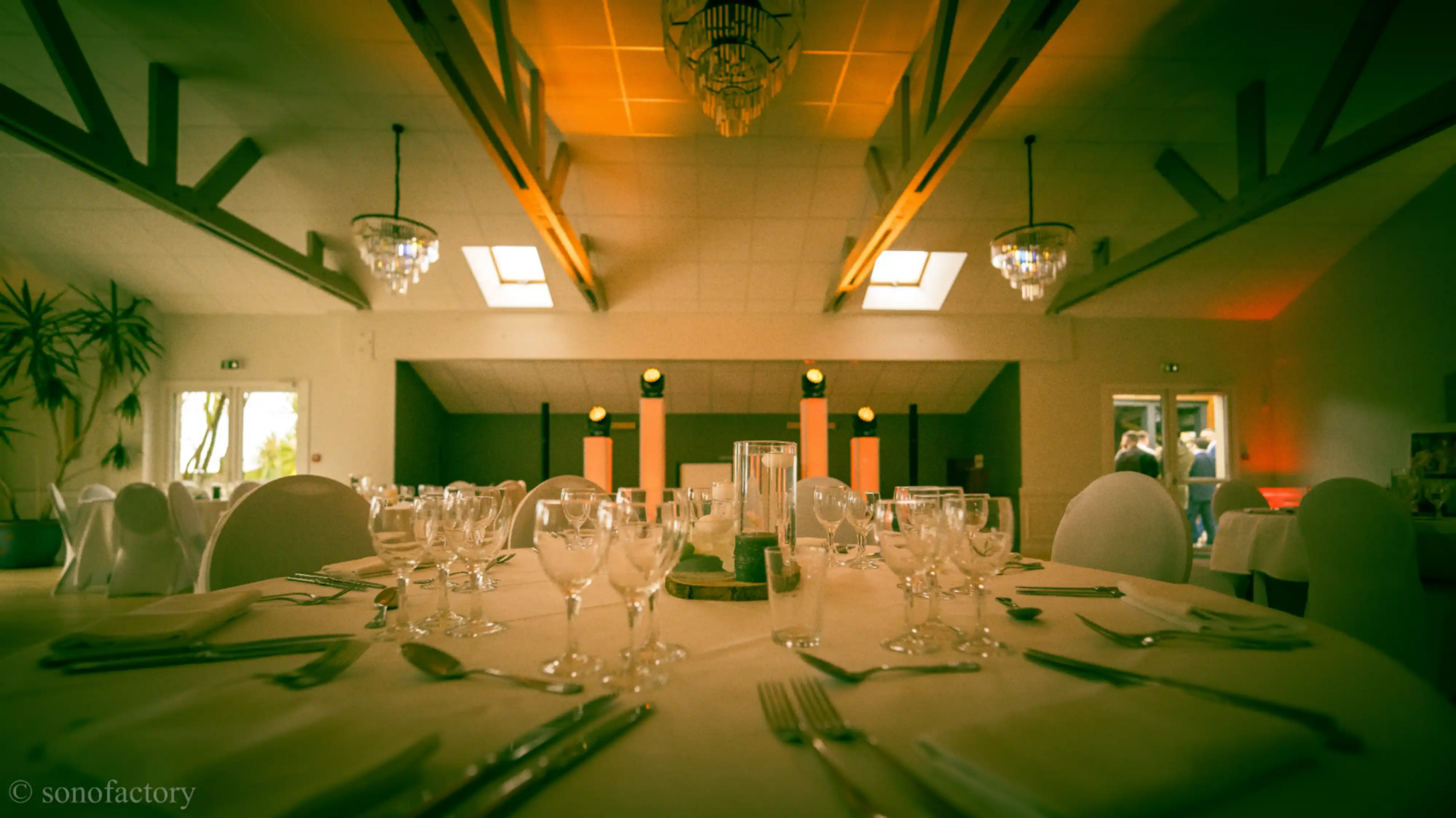 Salle de réception élégamment dressée pour un dîner d'entreprise en Bretagne, avec l'installation de la régie DJ et des totems lumineux par Sonofactory en arrière-plan.