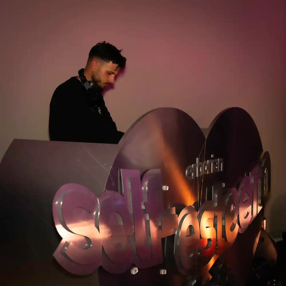 DJ professionnel en action lors d'une soirée d'entreprise en Bretagne, travaillant derrière une console décorative exclusive en forme de cœur avec le mot 'Self-Esteem' en relief